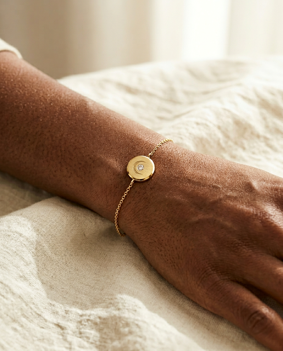 Lunar Bracelet on a Black woman's wrist resting on cream linen, fine 14K yellow gold cable chain with brushed medallion charm